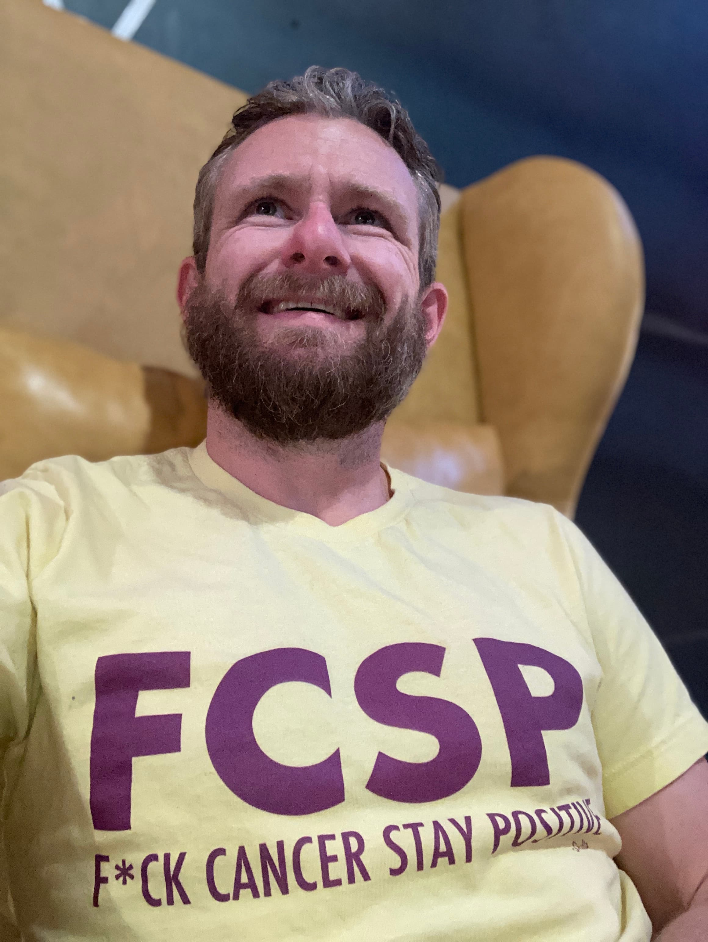 Troy Karnes in a yellow t-shirt, sitting in a leather chair