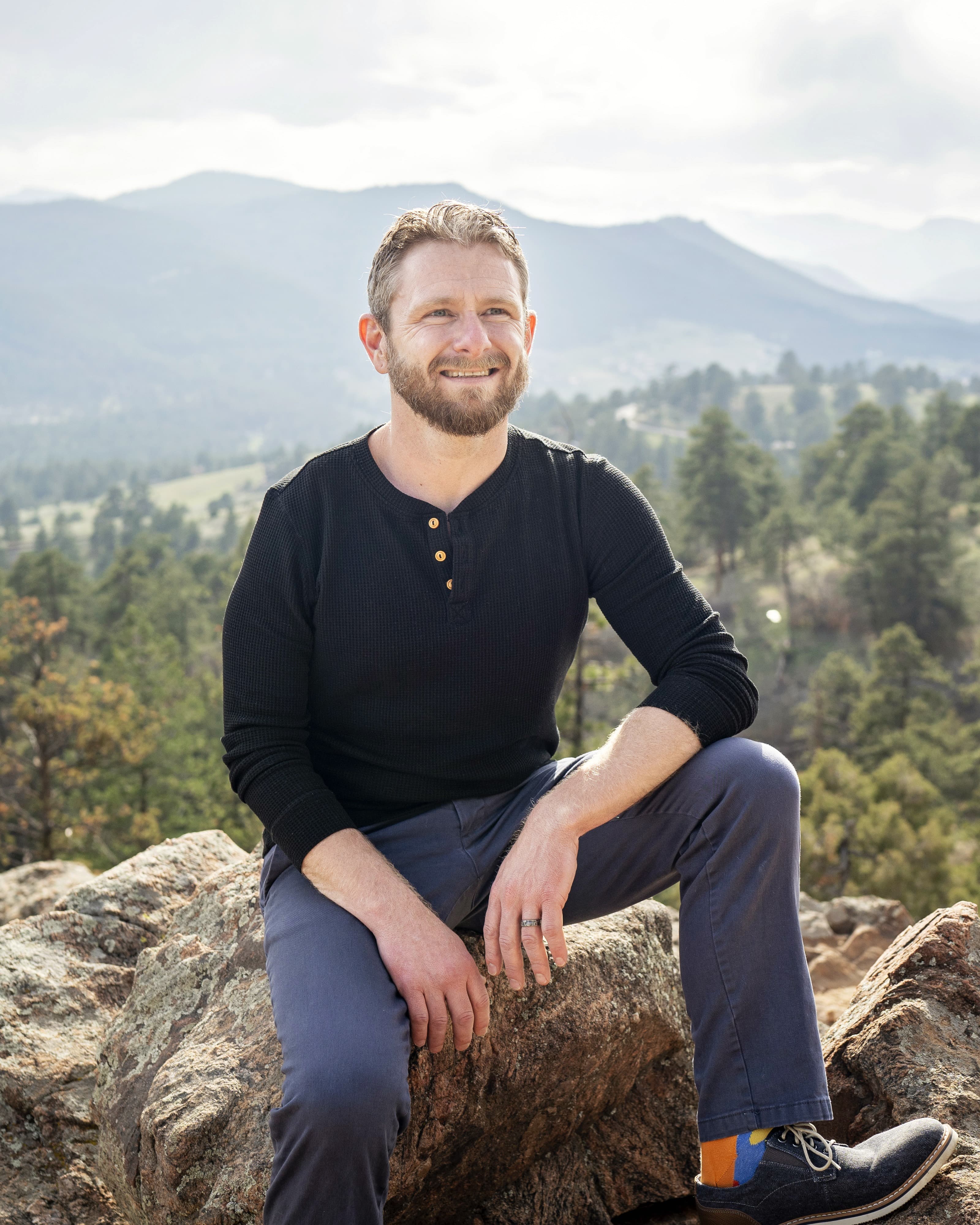 Troy Karnes sitting on a rock with the Colorado foothills behind him