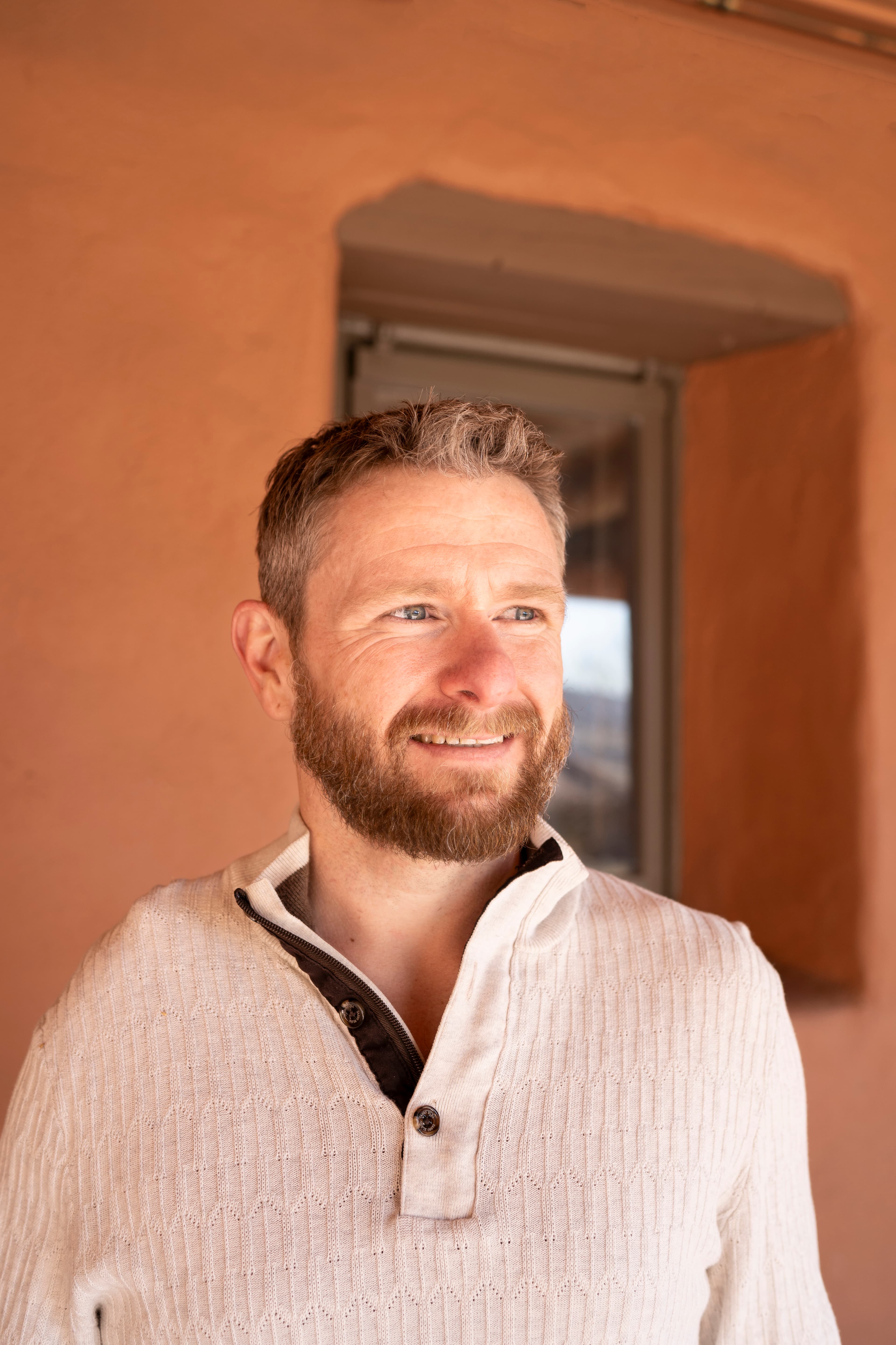 Troy Karnes against a warm adobe wall in a white sweater